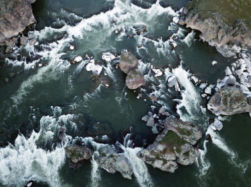 Aerial view of a river with white rapids and rocky outcrops surrounded by green vegetation.