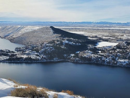 A scenic view of snow-covered mountains and a calm lake, with a clear sky in the background.