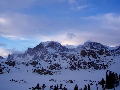 Snow-covered mountains under a cloudy sky, with patches of blue peeking through the clouds.