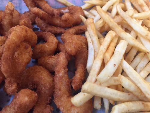 A close-up of crispy fried shrimp next to golden French fries on a tray.