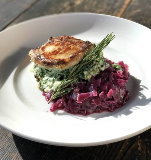A plated dish featuring a seared piece of fish atop creamy greens and a bed of red cabbage, garnished with rosemary.