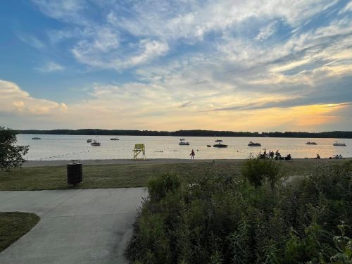 A serene beach scene at sunset with boats on the water and people enjoying the shore.