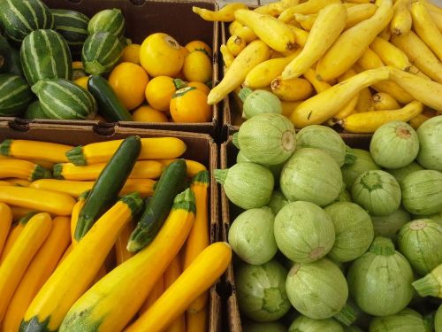 Colorful assortment of squash and zucchini in wooden crates, featuring yellow, green, and round varieties.