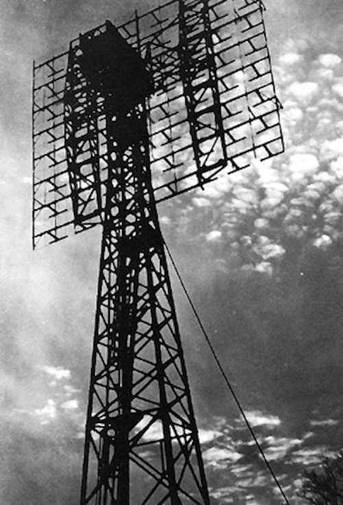 A tall radio tower with a grid-like structure against a cloudy sky, captured in black and white.