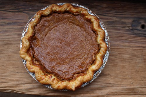 A freshly baked pumpkin pie in a silver pie dish, resting on a wooden surface.