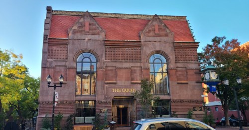 Historic building with a red-tiled roof, large windows, and decorative stonework, labeled "The Quoin."