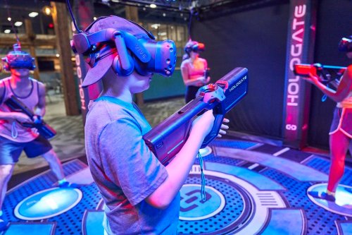 A group of people wearing VR headsets play a virtual reality shooting game in a high-tech arcade setting.