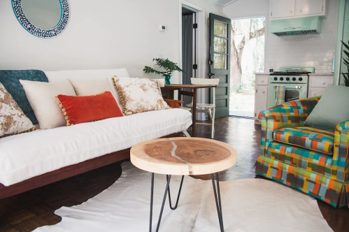 Cozy living room with a sofa, colorful chair, wooden coffee table, and a view of an outdoor space through an open door.