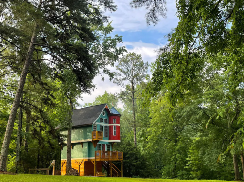 A colorful treehouse surrounded by lush green trees under a partly cloudy sky.
