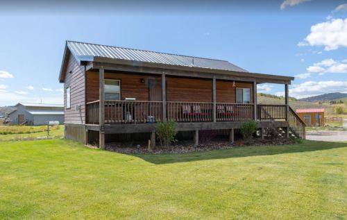 A wooden house with a porch, surrounded by green grass and a clear blue sky.