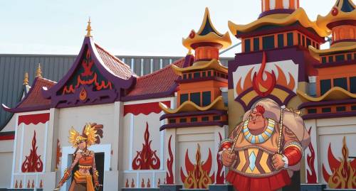 Colorful animated characters stand in front of a vibrant, flame-themed building with ornate architecture.