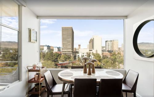 Modern dining area with a round table and chairs, featuring a large window showcasing a city skyline and mountains.