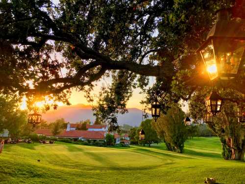 A scenic golf course at sunset, framed by trees and lanterns, with mountains in the background.