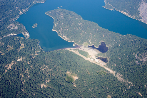 Aerial view of a lush, green landscape with a winding lake and small islands surrounded by dense forest.