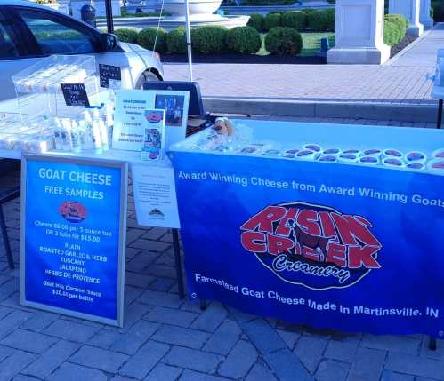 A vendor booth displaying goat cheese products and free samples, with a blue banner reading "Resin Creek Creamery."