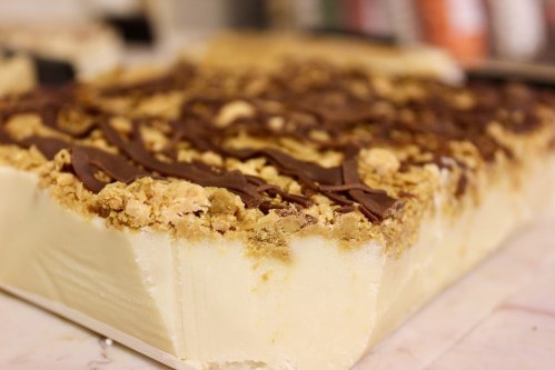A close-up of a dessert bar with a creamy base, topped with crumbled cookies and drizzled chocolate.