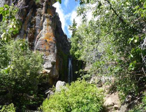 A serene waterfall cascading down rocky cliffs, surrounded by lush greenery and blue skies.