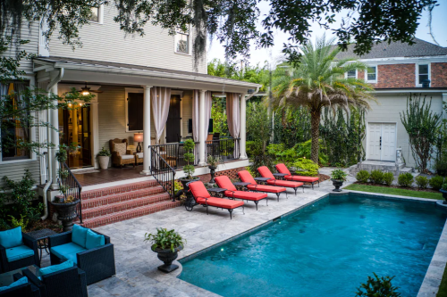 A serene backyard with a pool, lounge chairs, and a cozy porch surrounded by lush greenery.
