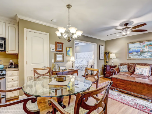 Cozy dining area with a glass table, wooden chairs, and a view of a living space featuring a sofa and artwork.