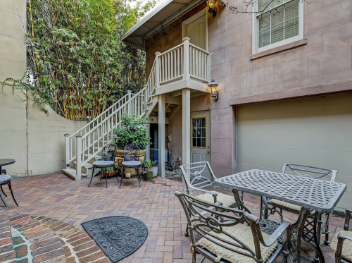 A cozy outdoor patio with a brick pathway, metal furniture, and a staircase leading to an upper level.