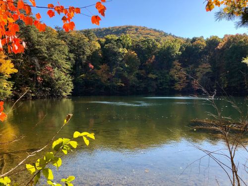 A serene lake surrounded by colorful autumn foliage and a distant hill under a clear blue sky.