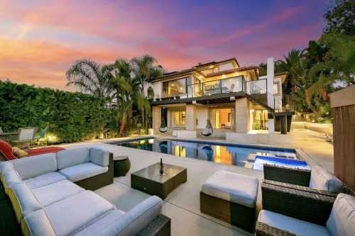 A luxurious backyard with a pool, lounge seating, and a modern home against a colorful sunset sky.