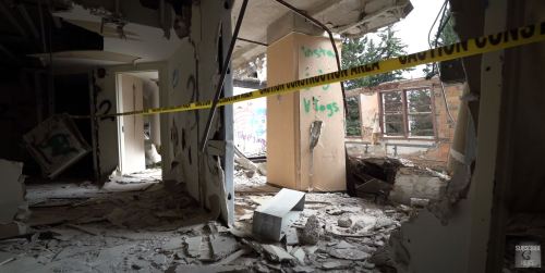 Interior of a dilapidated building with debris and caution tape, showing signs of damage and neglect.