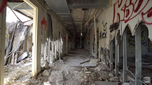 A dilapidated hallway in an abandoned building, with graffiti on the walls and debris scattered on the floor.