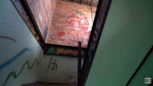 Graffiti on a brick wall inside a dimly lit, abandoned building with green walls and a staircase.