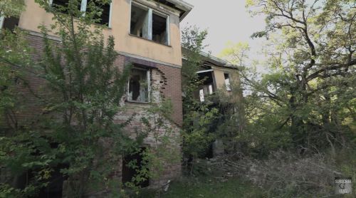 Abandoned building partially covered by overgrown vegetation, with broken windows and crumbling walls.