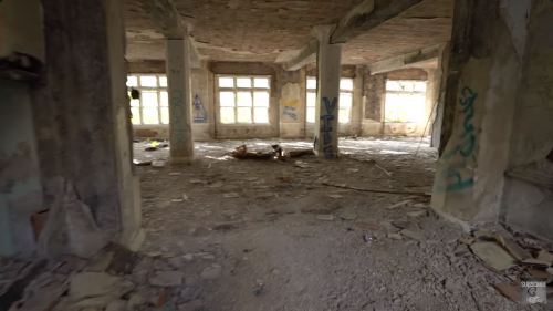 Abandoned interior of a building with debris, broken windows, and graffiti on the walls.