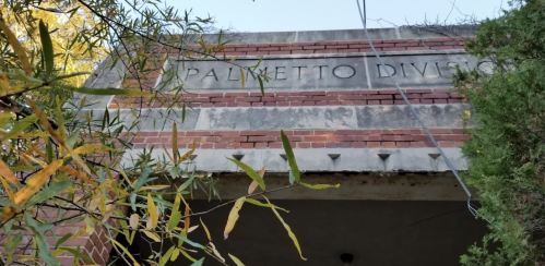 Close-up of a weathered brick structure with the words "Palmetto Division" engraved, surrounded by greenery.