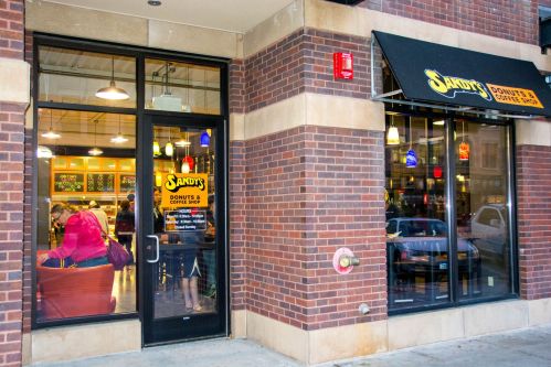 Exterior view of Sandy's Donuts & Coffee Shop, featuring a glass door and a black awning, with patrons inside.