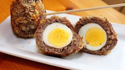 A plate with a sliced scotch egg, revealing a soft-boiled egg encased in seasoned meat and breadcrumbs.