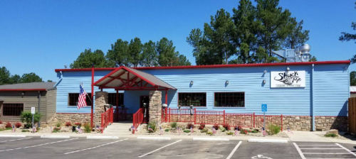 Exterior of a blue restaurant with a red roof, stone accents, and an American flag, surrounded by trees and a parking lot.