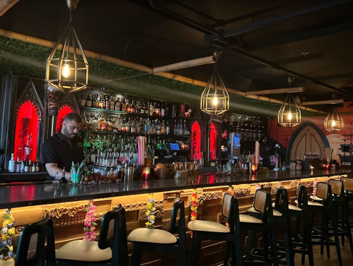 A stylish bar with a bartender, illuminated shelves of drinks, and decorative lighting in a vibrant setting.