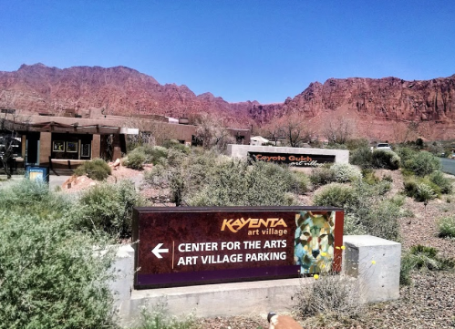 Sign for Kayenta Art Village and Center for the Arts, with red rock mountains in the background and desert vegetation.