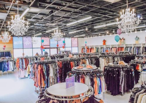 A spacious clothing store with racks of clothes, chandeliers, and colorful balloons, creating a vibrant shopping atmosphere.
