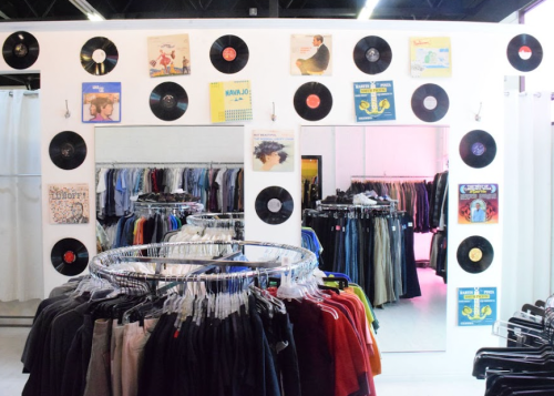 A thrift store interior featuring clothing racks and walls decorated with vinyl records and album covers.