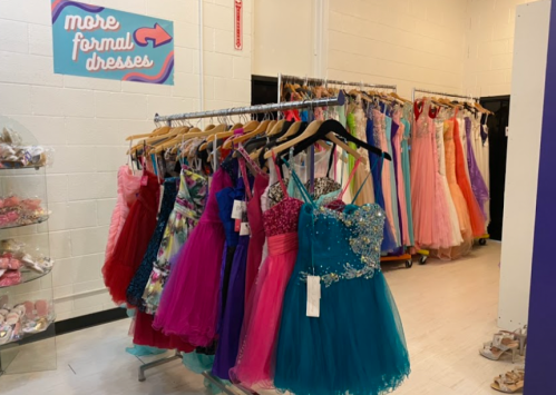 A rack of colorful formal dresses in a store, with a sign pointing to "more formal dresses" on the wall.