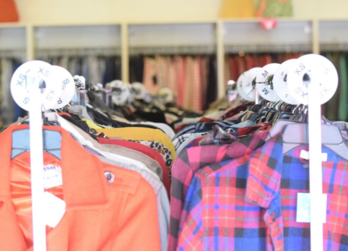 Clothes hanging on racks in a store, with size tags visible on the hangers.