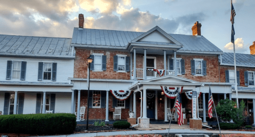 Historic brick building with a porch, decorated with flags and bunting, under a cloudy sky.