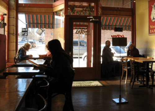 A cozy café interior with patrons seated at tables, enjoying their time, and sunlight streaming through the windows.