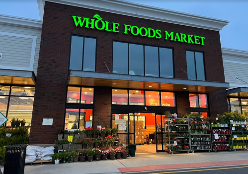 Exterior of a Whole Foods Market with bright green signage and a display of plants and flowers at the entrance.
