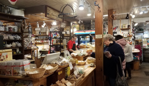 A cozy shop filled with baked goods and treats, featuring customers browsing and a staff member at the counter.