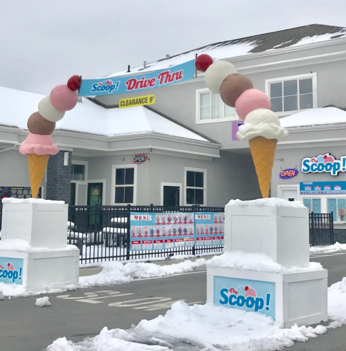 Two large ice cream cone sculptures stand outside a drive-thru shop, with snow covering the ground.