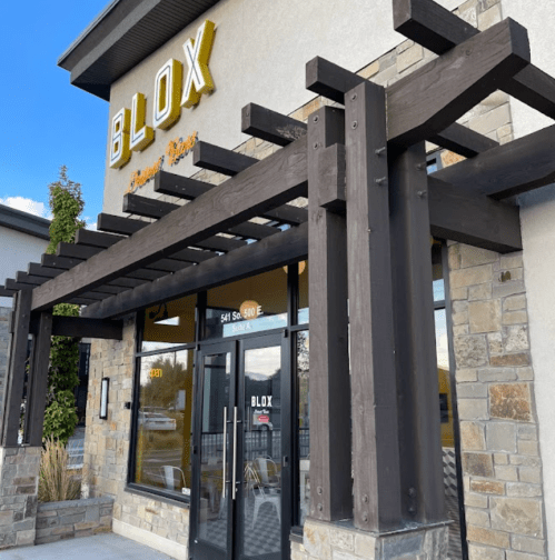 Exterior of Blox restaurant featuring a wooden pergola and stone facade, with large glass doors and a clear sky above.