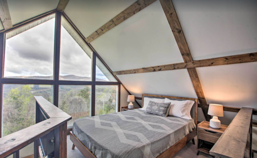 Cozy bedroom with a large window showcasing a mountain view, featuring wooden beams and modern decor.