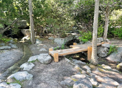 A wooden bridge over a small stream in a serene garden surrounded by rocks and greenery.