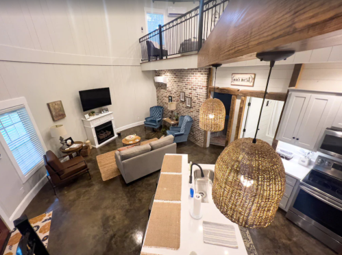 A spacious, modern living area with a kitchen, cozy seating, and a lofted space above, featuring warm lighting and decor.